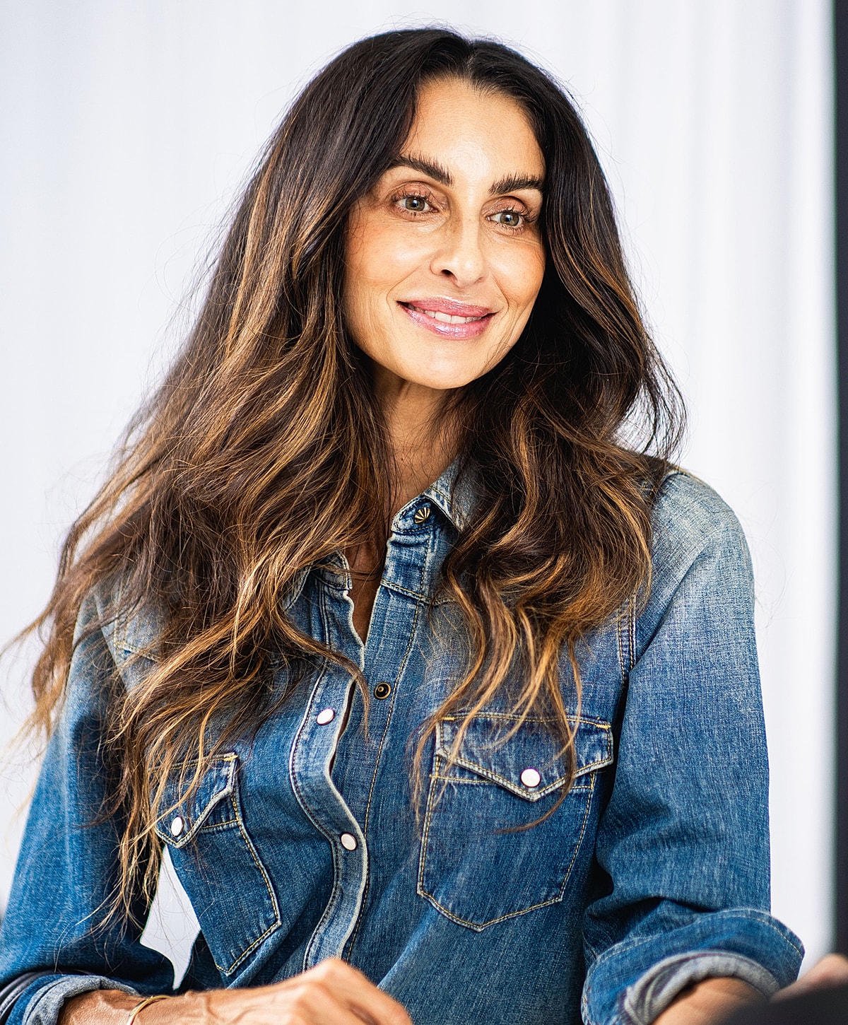 Smiling woman with long hair in denim shirt.