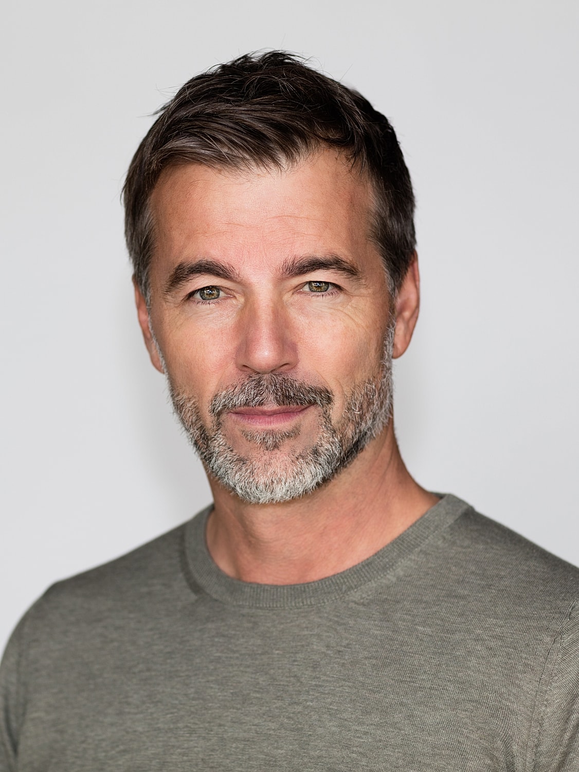Smiling man with beard in gray shirt.