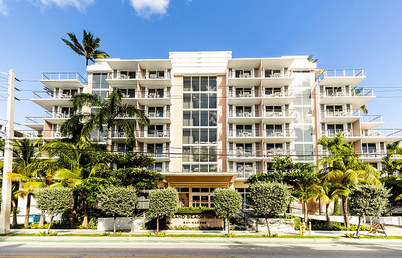 Modern hotel with palm trees under bright sky.