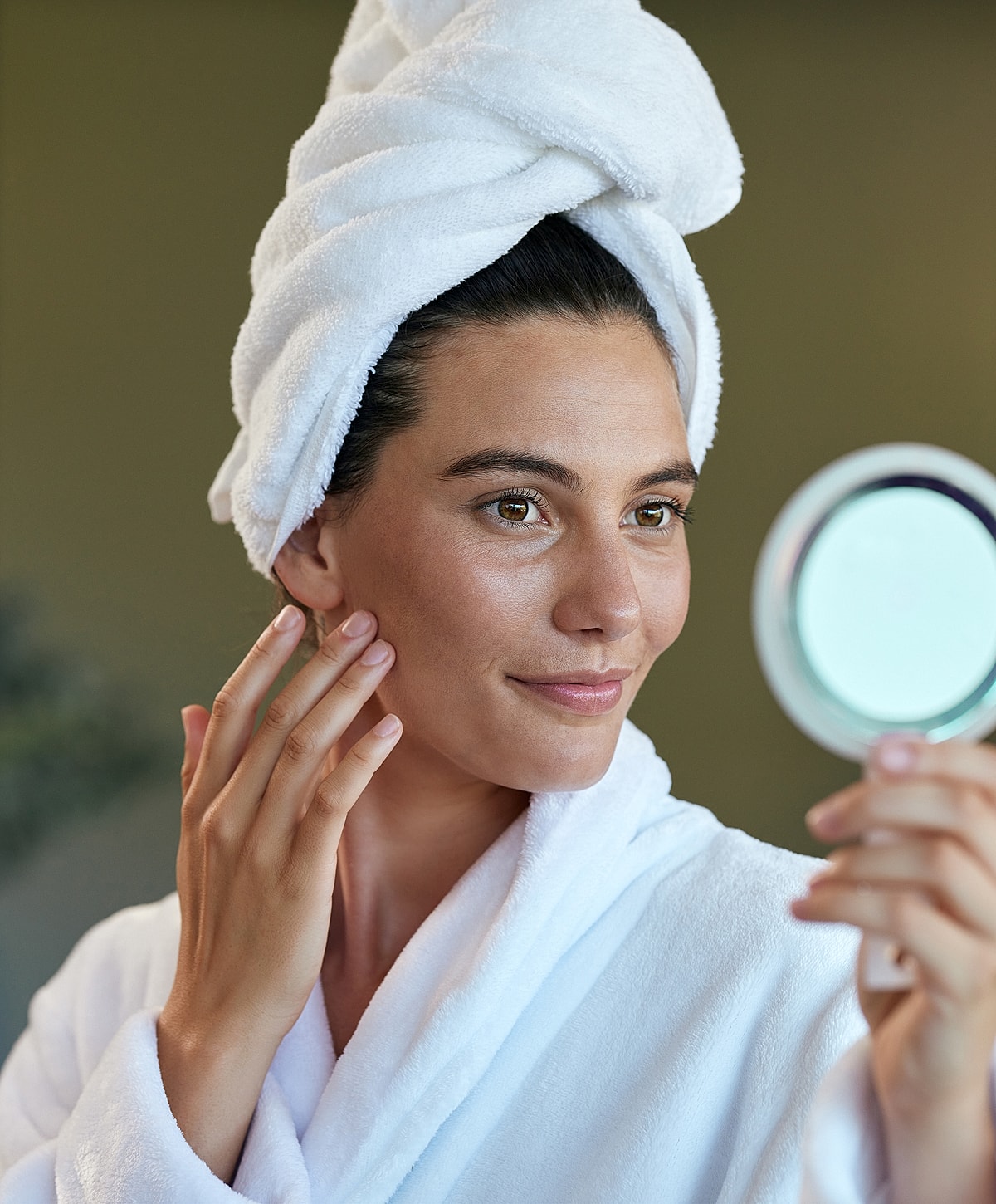 Woman applying skincare while looking in mirror.