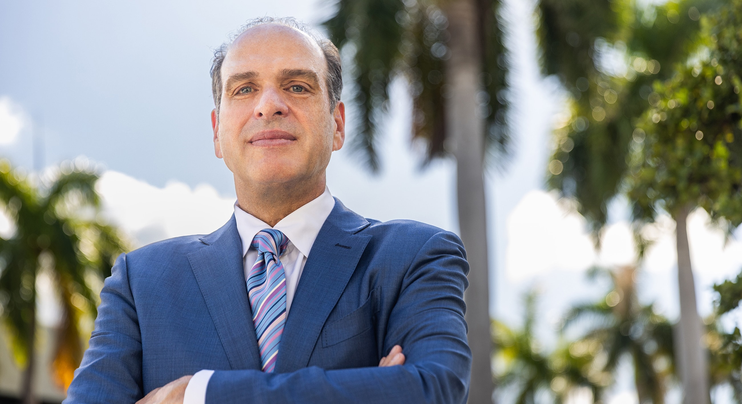 Man in suit standing confidently outdoors among trees.