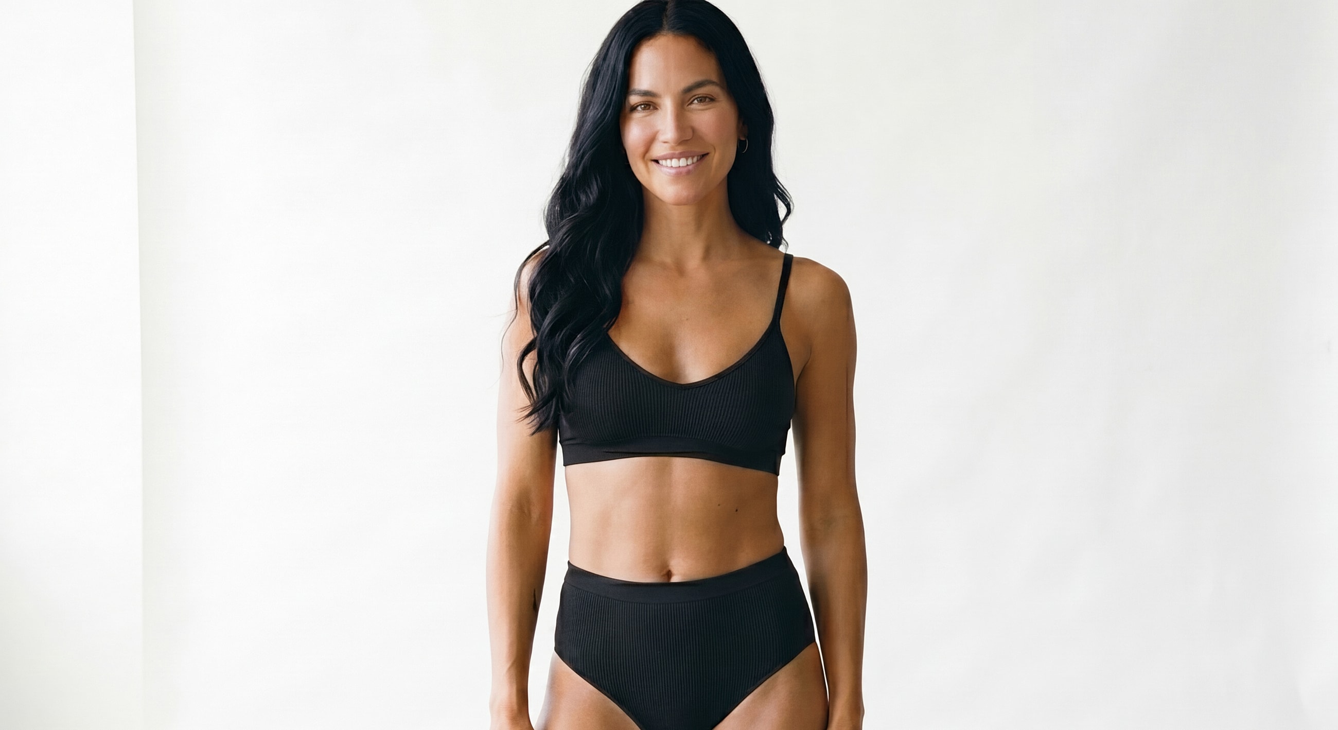 Woman in black bikini smiling against white background