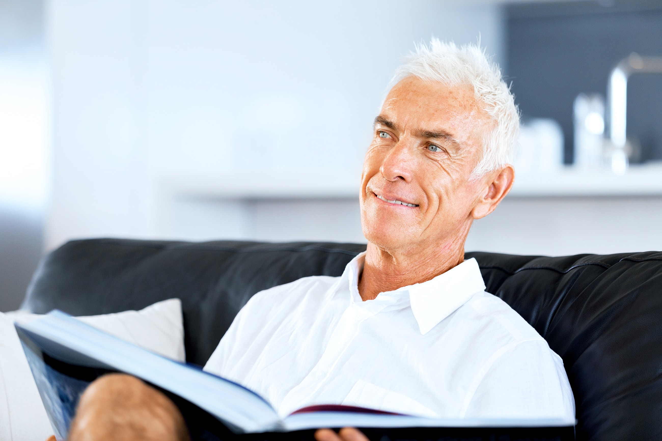 Older man reading a book on a couch.