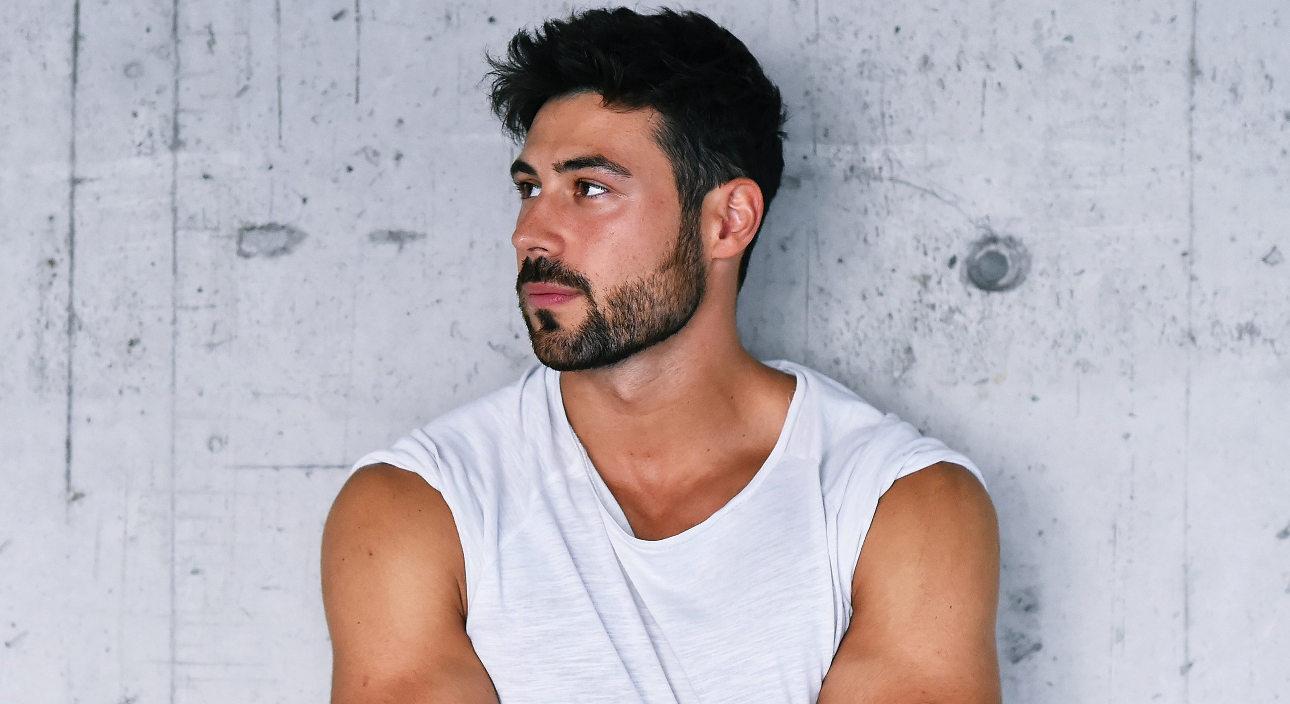 Man in a sleeveless shirt against a concrete wall.