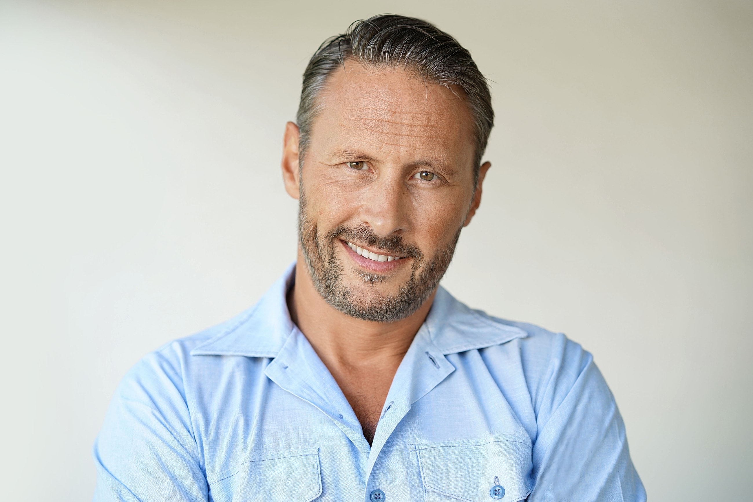 Smiling man in light blue shirt, neutral background.
